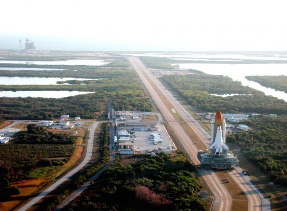在5.5公里長的履帶車道上，履帶式運輸裝置正在運輸移動式發射台，前往畫面左前方的39A發射台。來源：NASA.